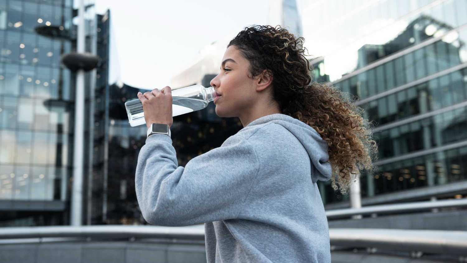 Mujer bebiendo agua de un botella de cristal mientras hace deporte