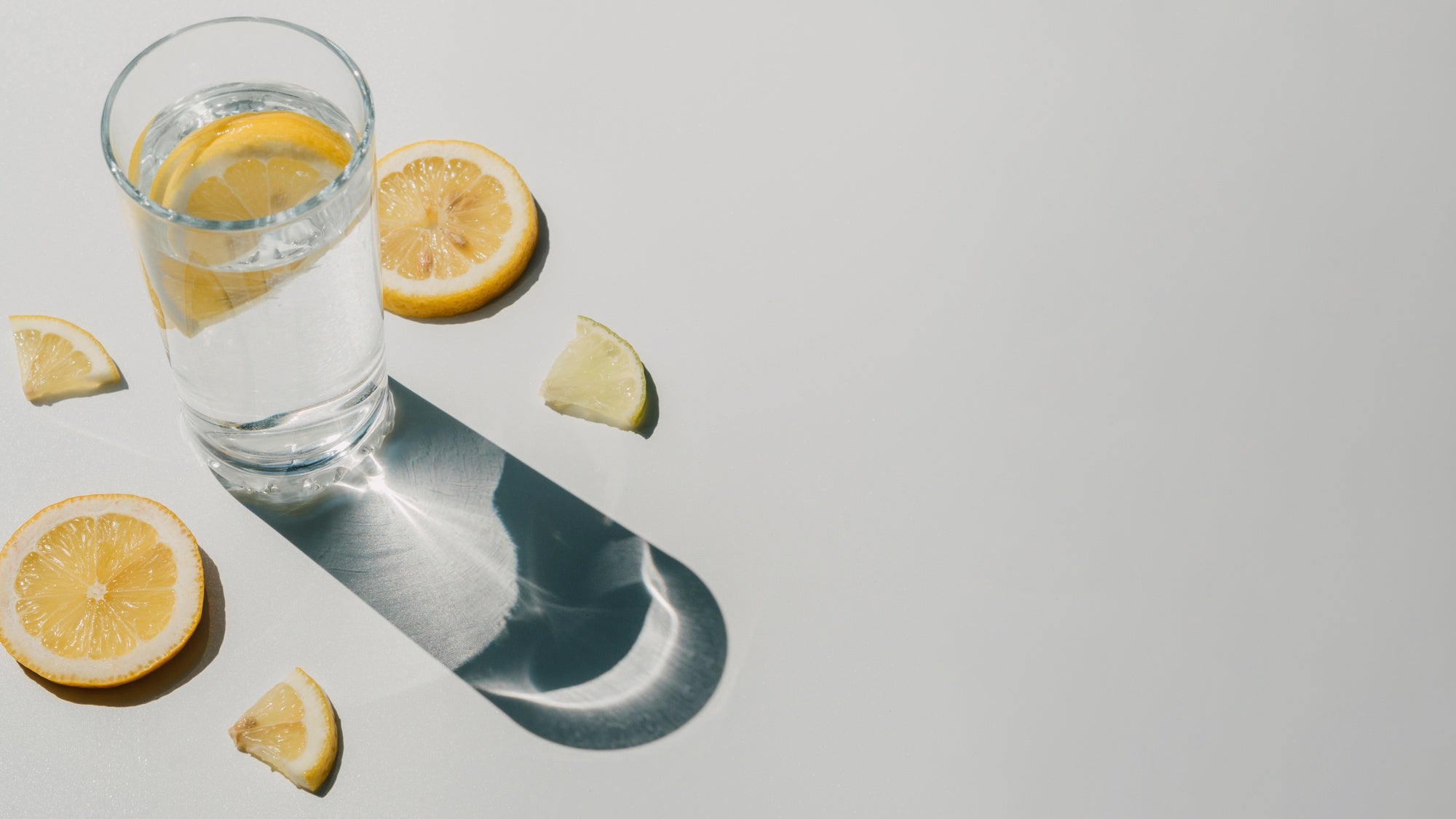 Vaso de agua con limones en fondo blanco
